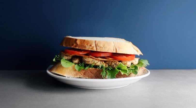 Chicken BLT sandwich on white plate with blue background - 810 x 450