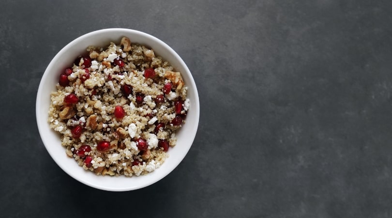 Low FODMAP Pomegranate Quinoa Salad in white bowl on grey surface - 810 x 450