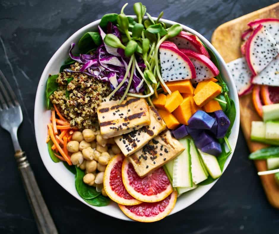 White bowl with fresh fruit, quinoa, and tofu