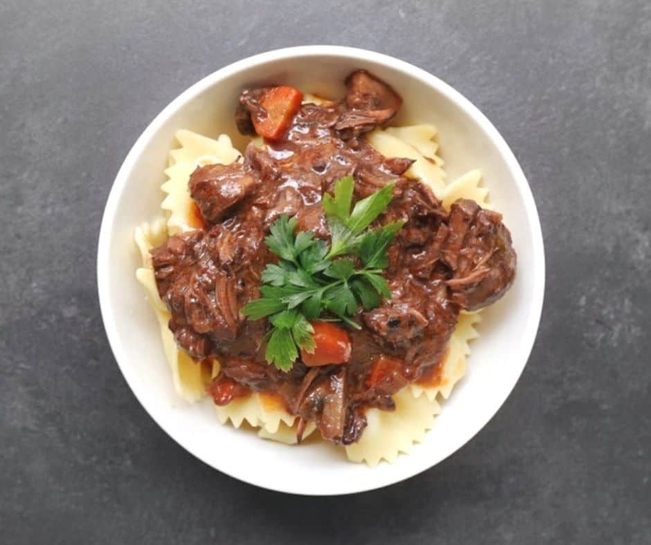 beef bourguignon over noodles in white bowl