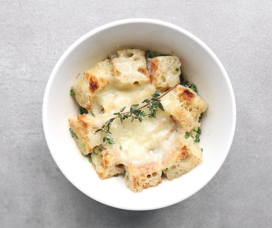 Low FODMAP french onion soup in white bowl with bread cubes and cheese